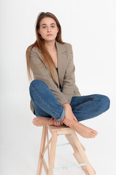 portrait of young attractive caucasian woman with long brown hair in suit jacket. skinny pretty lady sitting on wooden ladder with bare feet. model tests of beautiful lady