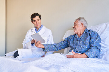 Senior patient in bed shows male nurse the tablet PC