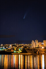 Fototapeta na wymiar Comet Neowise over Rijeka port city on Adriatic sea, Croatia. Amazing night cityscape with city lights, blue starry sky and reflection in the water, outdoor travel and scientific background
