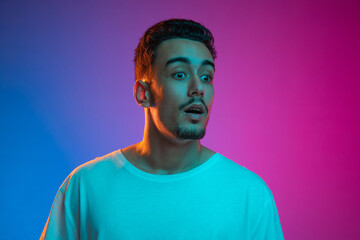 Portrait of Latina young man posing isolated on gradient purple pink background in neon light....