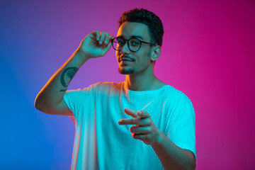 Portrait of Latina young man posing isolated on gradient purple pink background in neon light. Front view - obrazy, fototapety, plakaty