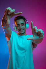 Portrait of Latina young man in white headphones posing isolated on gradient purple pink background...
