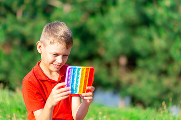 8 year old boy in red t-shirt plays with eternal bubble wrap in the park and smiles while sitting on a blanket on a background of greenery outdoors