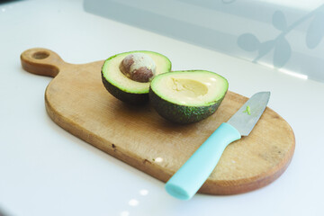 Cut avocado into two pieces on a wooden kitchen board with a knife. Photo for step by step avocado salad recipes. The concept of cooking, proper healthy nutrition, vitamins.