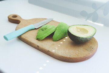 Cut avocado into thin slices on a wooden kitchen board with a knife. Photo for step by step avocado salad recipes. The concept of cooking, proper healthy nutrition, vitamins.