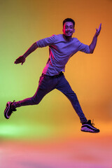 Fototapeta na wymiar Full length portrait of Latina young man jumping high isolated on gradient yellow green background in neon light.