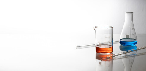 Two laboratory glass bottles and chemical liquids, pipettes on the glass table.Empty space
