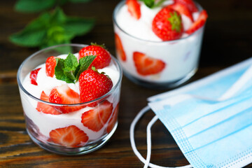 Whipped cream and strawberries served in a glass. Dark wooden table, surgical masks, high resolution