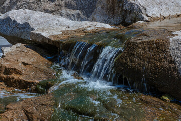 Selective focus close-up of clear stream water running over large rocks. Water running through a...