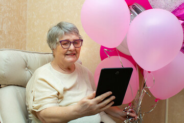 Cheerful elderly lady with balloons receives birthday greetings online