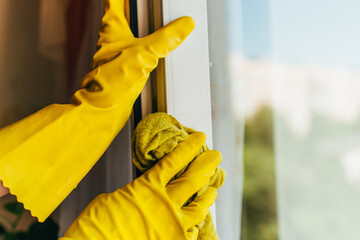 A person wearing yellow gloves to clean the window from dirt with a special rag