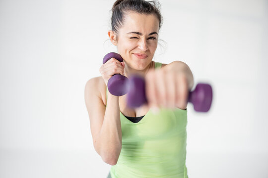 Portrait of a beautiful and confident athletic woman exercising with dumbbells at white room. Training fitness or aerobics
