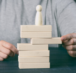 woman's hand pulls out a wooden block from the tower on which the figurine stands. The concept of...