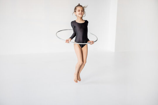 Portrait of a happy little girl jumping with gimnastic ring at white room. Children's gymnastics and training from an early age
