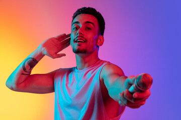 Portrait of Latina young man, singer with microphone performing isolated on gradient yellow purple...