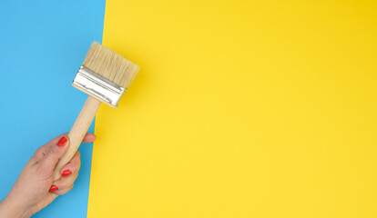 female hand hold new paint brush with wooden handle on a yellow background