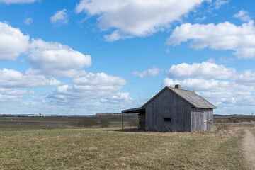 An old abandoned small wooden house in the fields sky clouds, barn or scary concept.