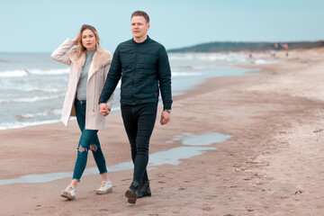 Attractive young couple walking along the shore of a sandy beach, on a spring romantic holiday, outdoors.