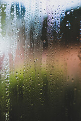 water droplets of humidity condensation on window seen from indoor with backyard bokeh in the background
