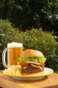 A close shot of a blonde lager beer, pototo chips, and a hamburger
