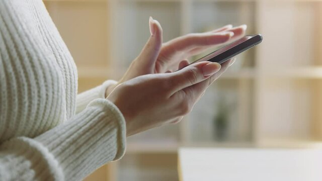 Internet addiction. Modern generation. Digital lifestyle. Mobile technology. Virtual life. Unrecognizable woman fast scrolling liking in smartphone light room interior.
