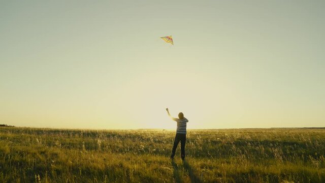 A happy girl with a kite in her hands runs across the field in the rays of the sunset. A carefree child dreams of freedom, flight. Teenager playing with an airplane outdoors in park, wants to be pilot