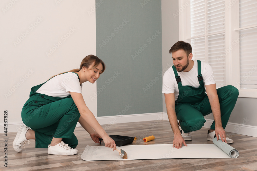 Poster Workers applying glue onto wall paper sheet on floor indoors