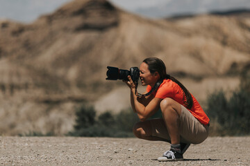Woman photographer taking photos in Tabernas Desert, Spain, in a sunny day, with an orange color t-shirt.