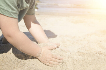A small child plays on the beach on a summer day. The child builds a slide out of sand. Copy space.