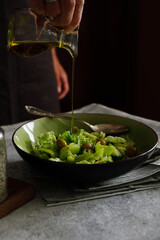 a man prepares a vegetable salad on a dark background. Dark photo style. Adds olive oil