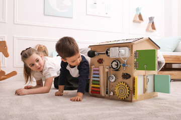 Little boy and girl playing with busy board house on floor in room