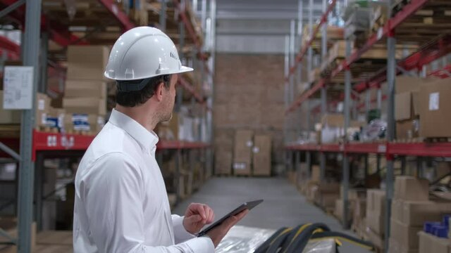 Employee male warehouse worker engineer man in hard hat working at construction site warehouse, walking in logistics center factory, storekeeper using tablet computer, architect businessman indoors
