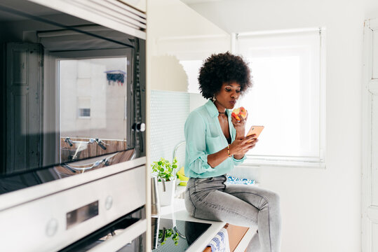 Young black woman eating apple in kitchen