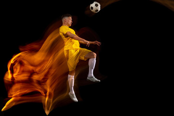 Obraz na płótnie Canvas Young caucasian male football or soccer player training in mixed light isolated on dark background. Concept of healthy lifestyle, professional sport, active, motion..