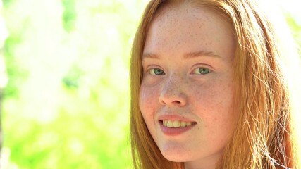 Portrait a smiling young woman with red hair and freckles against the backdrop of a bright sunny...