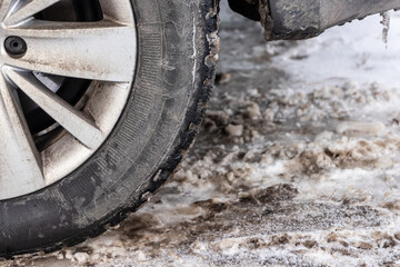 Close up photo of detail of car back wheel with dirty tire during snowy winter day. Part of car bumper, tire and wheel disk with dirt during winter