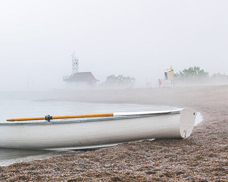 Traditional wooden rowboat sitting on a beach in fog with traditional wooden oars.  Shot in the Toronto Beaches in June.