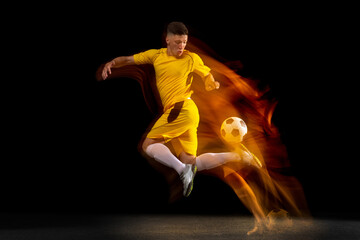 Fototapeta na wymiar One caucasian male football or soccer player training with ball in mixed light isolated on dark background. Concept of professional sport, active, motion..