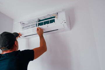 Service and maintenance of the air conditioner. A young male technician is cleaning and replacing...