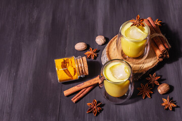 Golden turmeric milk with ice on black wooden background