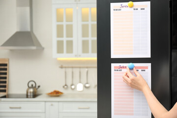 Woman putting blank to do list on refrigerator door in kitchen, closeup. Space for text