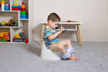 A small child sits on a pot and watches cartoons on his phone. Learning to pot, dependence on...