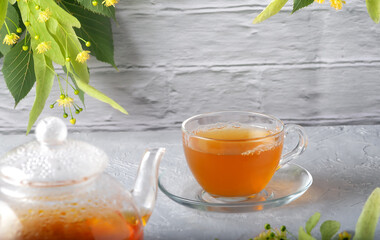 Teapot and cup with linden tea and flowers on a wooden table against a brick wall background
