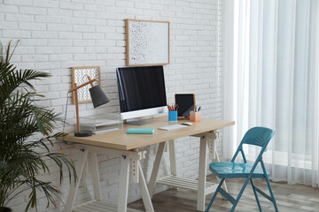 Stylish home office interior with comfortable workplace near white brick wall