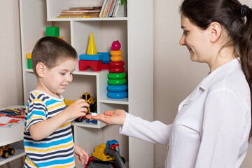 A female pediatrician or nurse gives a child a white vitamin pill. Dietary supplements for...
