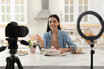 Blogger with tasty cake recording video in kitchen at home. Using ring lamp and camera