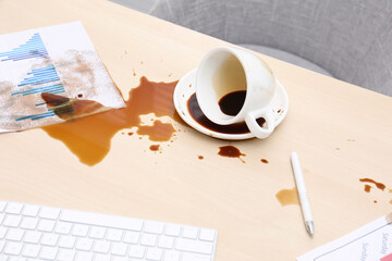 Cup with saucer and coffee spill on wooden office desk