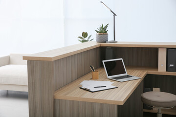 Stylish modern wooden desk with laptop indoors. Receptionist workplace