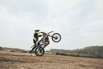 Fototapeta na wymiar Motorcyclist jumping and riding on rear wheel at enduro motocross training ground