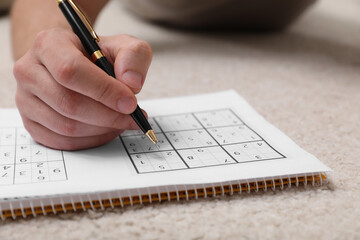 Man solving sudoku puzzle on floor at home, closeup